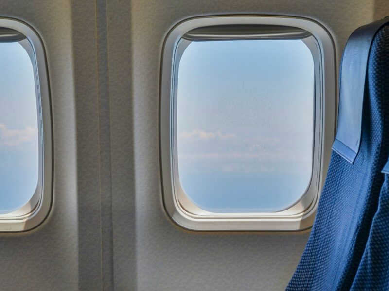 Blaue Flugzeugsitze neben zwei Kabinenfenstern mit Blick auf Himmel und Wolken