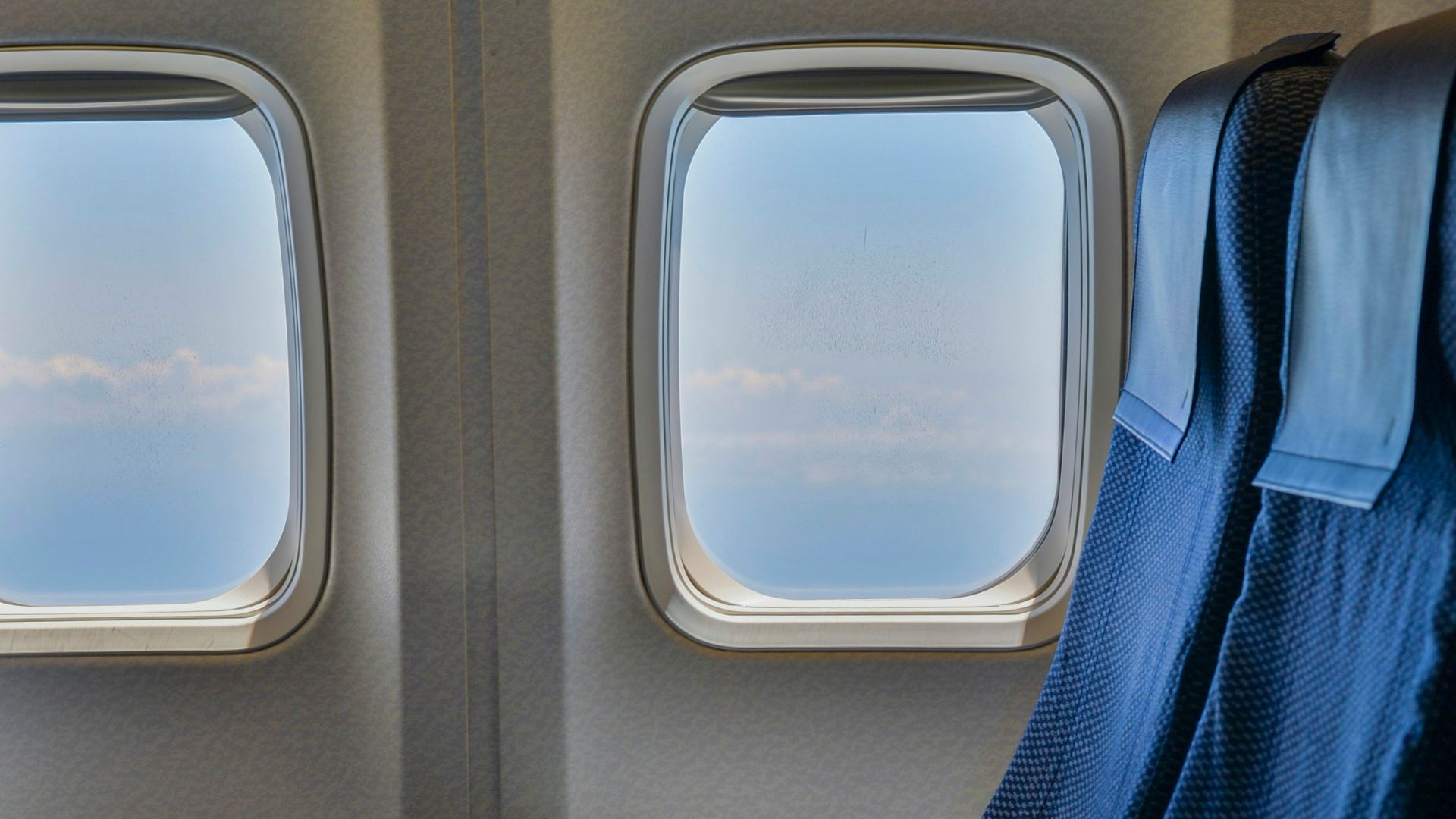 Blaue Flugzeugsitze neben zwei Kabinenfenstern mit Blick auf Himmel und Wolken